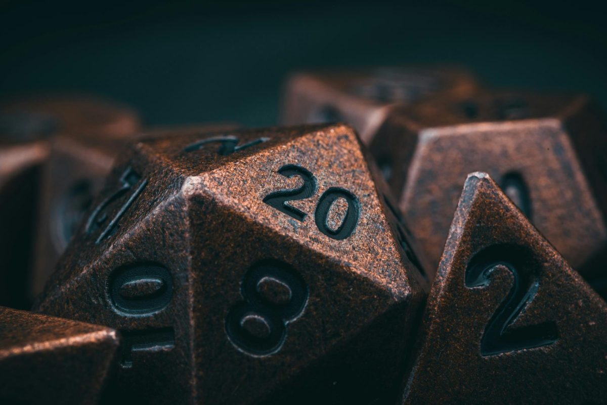 A group of umber dice with engraved numbers on each face, focusing on a 20. Image used from Unsplash. (Timothy Dykes)